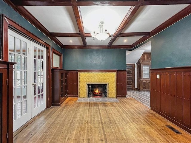 unfurnished living room featuring french doors, coffered ceiling, light hardwood / wood-style flooring, a notable chandelier, and beamed ceiling
