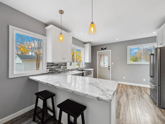 kitchen with kitchen peninsula, stainless steel fridge, plenty of natural light, and white cabinets