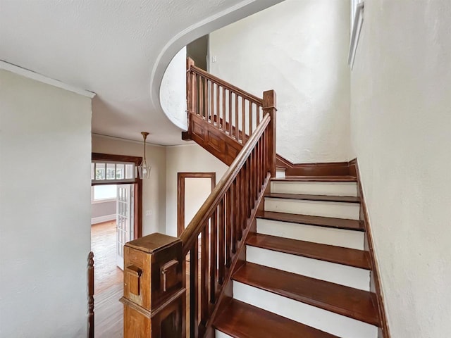 staircase with hardwood / wood-style floors, a textured ceiling, and crown molding