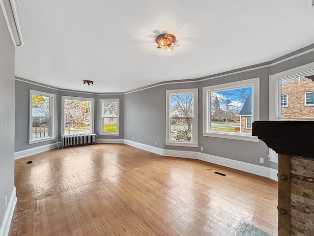 unfurnished living room with radiator heating unit, ornamental molding, and light hardwood / wood-style flooring