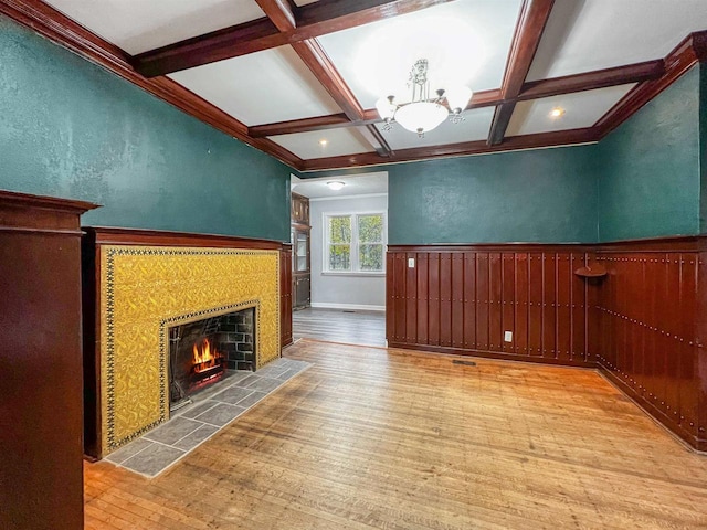 unfurnished living room with coffered ceiling, beam ceiling, a tiled fireplace, and light hardwood / wood-style flooring