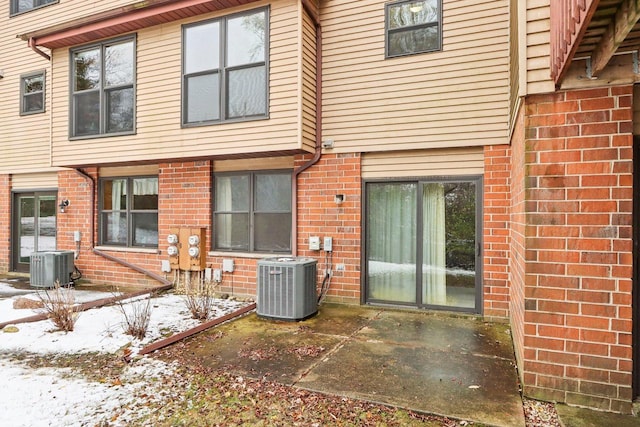 snow covered house featuring central AC unit and a patio area