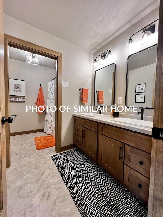 full bath featuring double vanity, baseboards, and a sink