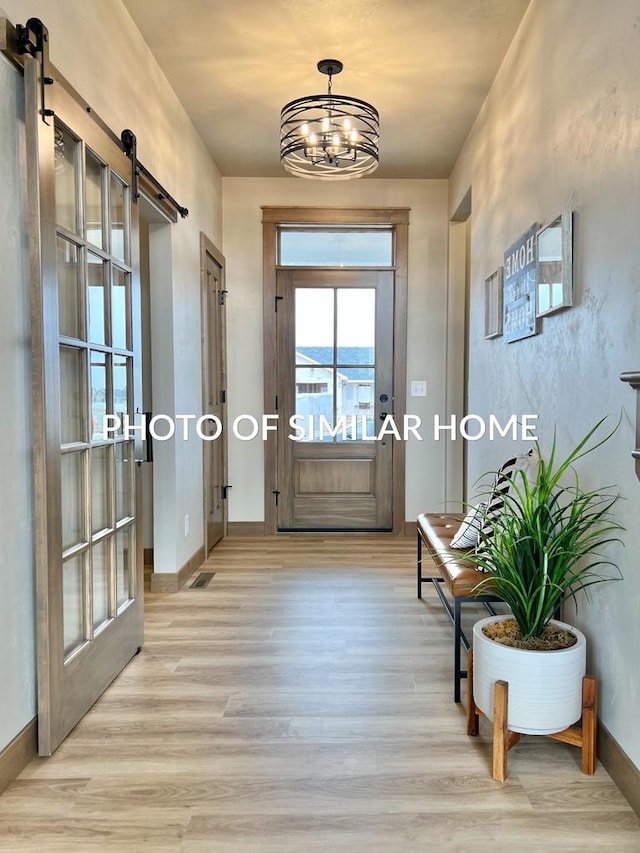 entryway with a barn door, light hardwood / wood-style floors, and a notable chandelier