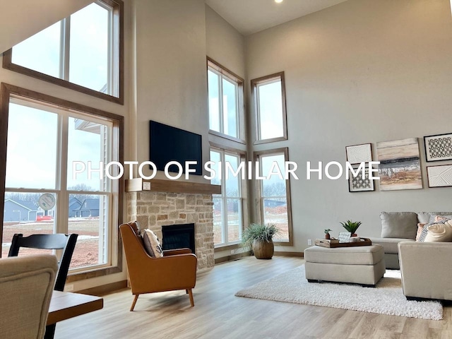 living room featuring a high ceiling, light hardwood / wood-style flooring, and a stone fireplace