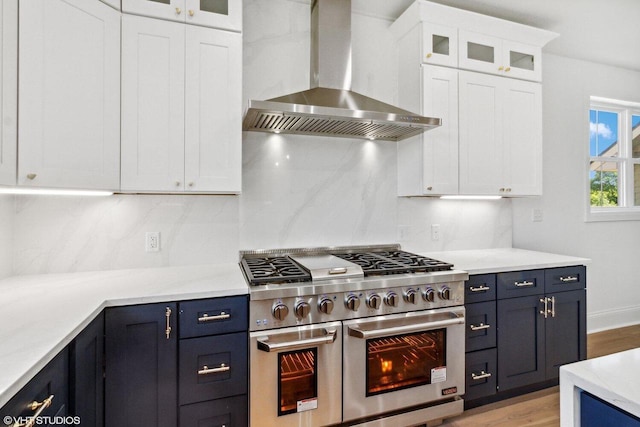 kitchen with white cabinets, wall chimney exhaust hood, range with two ovens, and blue cabinets