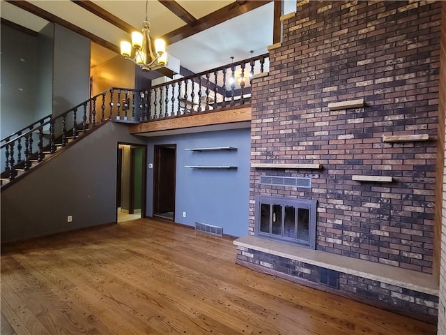 unfurnished living room featuring beam ceiling, a brick fireplace, a notable chandelier, hardwood / wood-style floors, and a towering ceiling