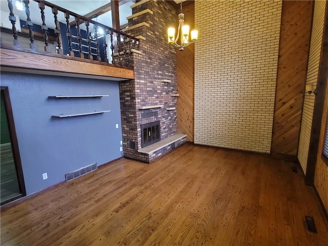 unfurnished living room featuring hardwood / wood-style floors, a notable chandelier, a large fireplace, and a high ceiling