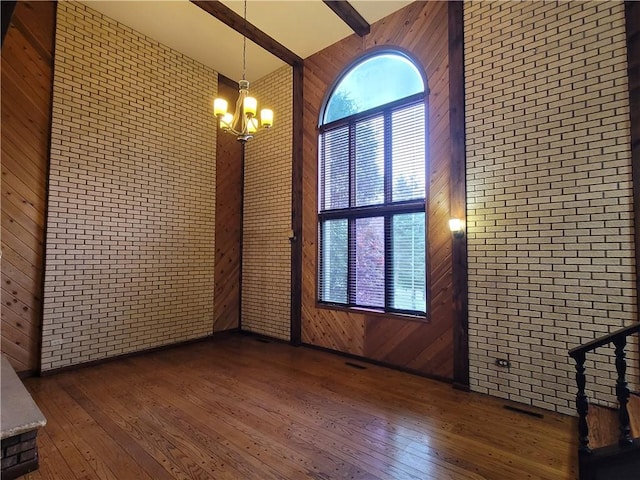 unfurnished room featuring dark hardwood / wood-style flooring, a towering ceiling, and brick wall