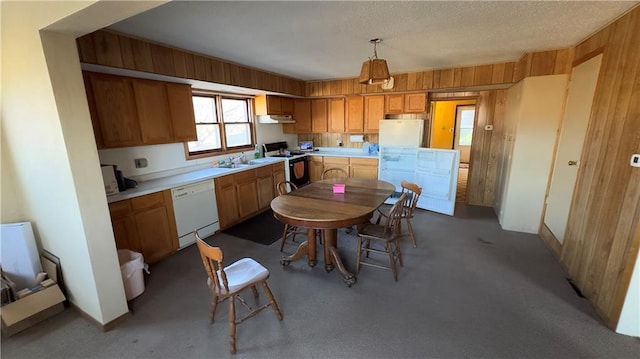 kitchen with a textured ceiling, white appliances, decorative light fixtures, and wood walls