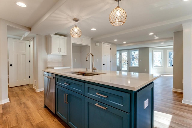 kitchen featuring stainless steel dishwasher, sink, blue cabinetry, white cabinets, and an island with sink