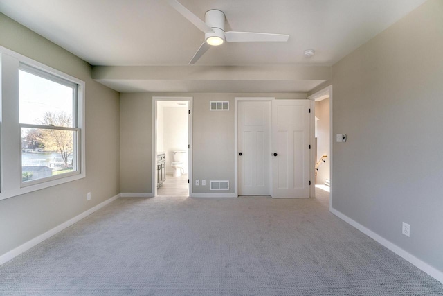 unfurnished bedroom featuring light carpet, a closet, ensuite bath, and ceiling fan