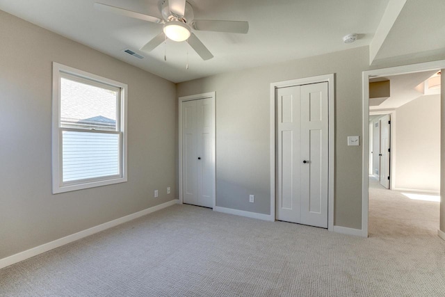 unfurnished bedroom with light carpet, ceiling fan, and multiple closets