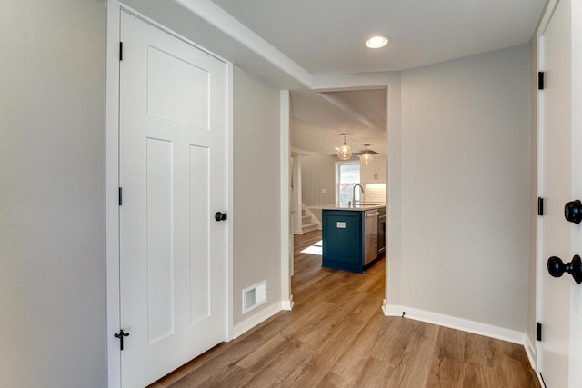 corridor with light hardwood / wood-style flooring, a notable chandelier, and sink