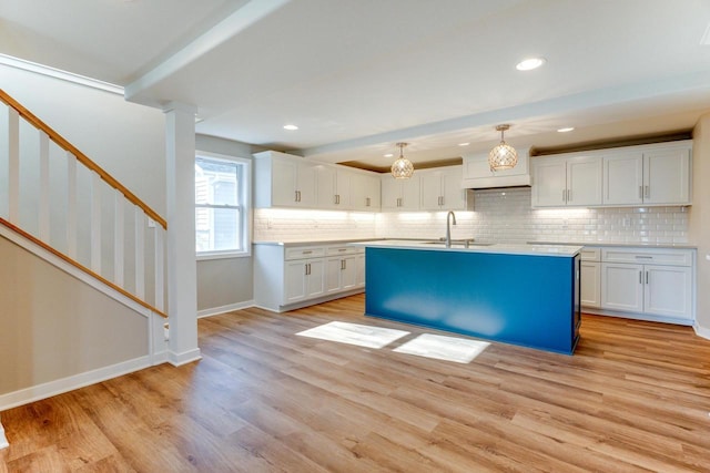 kitchen featuring sink, tasteful backsplash, light hardwood / wood-style floors, decorative light fixtures, and white cabinets