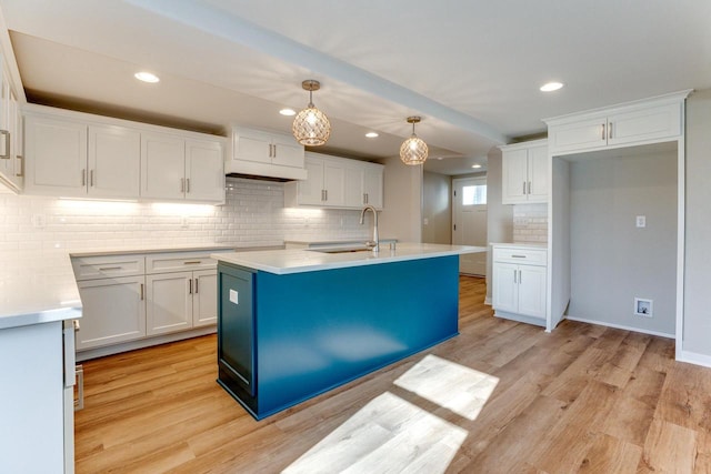 kitchen featuring white cabinets, light wood-type flooring, decorative light fixtures, and sink