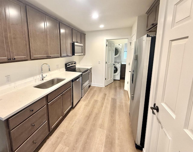 kitchen featuring sink, stainless steel appliances, light hardwood / wood-style flooring, stacked washer / dryer, and dark brown cabinets