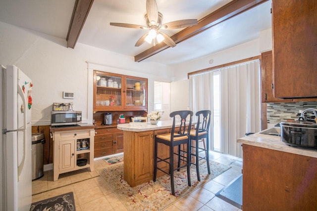 kitchen featuring white refrigerator, ceiling fan, decorative backsplash, beam ceiling, and a breakfast bar area