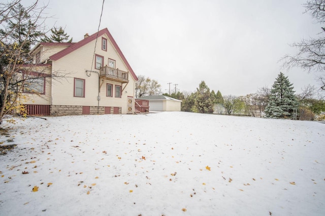 snow covered back of property with a balcony, a garage, and an outdoor structure