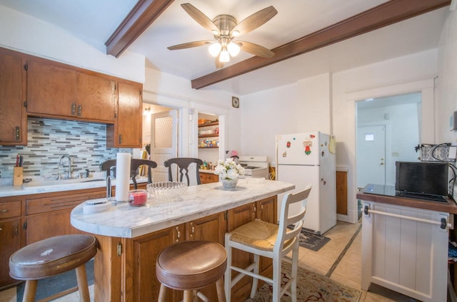 kitchen with ceiling fan, sink, backsplash, white fridge, and a breakfast bar