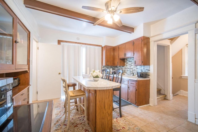 kitchen with ceiling fan, sink, decorative backsplash, a breakfast bar, and light tile patterned floors