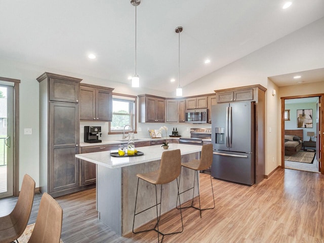 kitchen with a center island, pendant lighting, lofted ceiling, appliances with stainless steel finishes, and light wood-type flooring