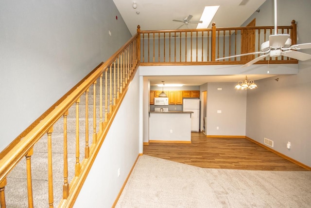 stairway featuring a towering ceiling, hardwood / wood-style floors, and ceiling fan with notable chandelier