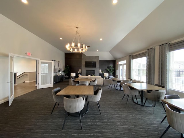 dining space with a large fireplace, a healthy amount of sunlight, vaulted ceiling, and an inviting chandelier