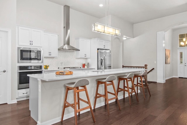 kitchen with stainless steel appliances, white cabinetry, a large island, and wall chimney range hood