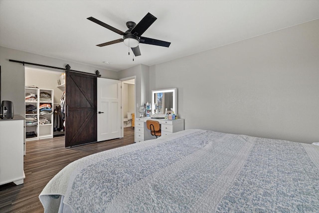 bedroom featuring a walk in closet, a barn door, ceiling fan, and dark wood-type flooring