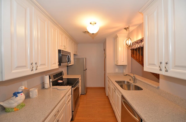 kitchen with sink, stainless steel appliances, pendant lighting, light hardwood / wood-style floors, and white cabinets