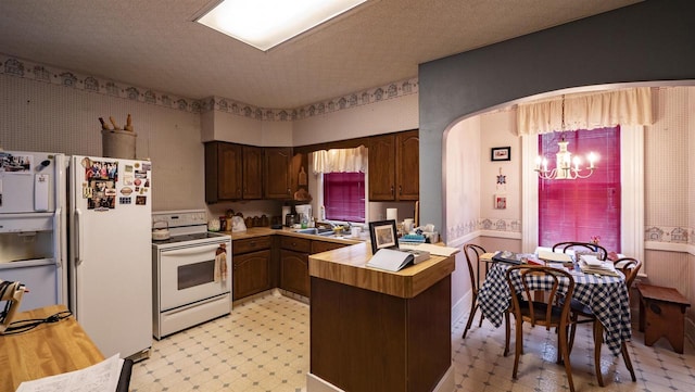 kitchen with white appliances, kitchen peninsula, a textured ceiling, a notable chandelier, and dark brown cabinets