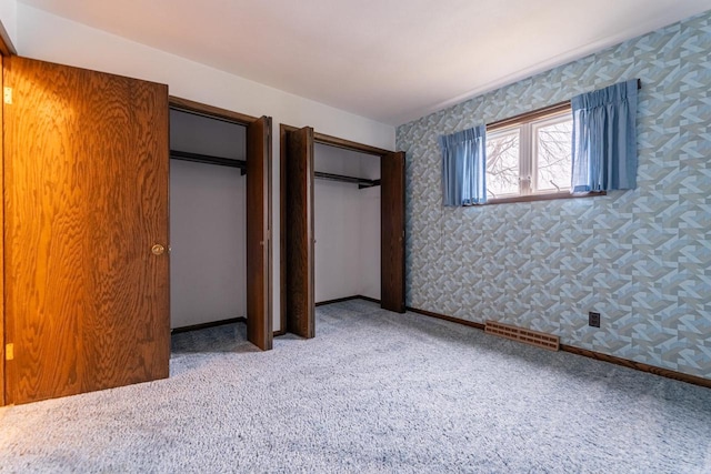 unfurnished bedroom with light colored carpet and multiple closets