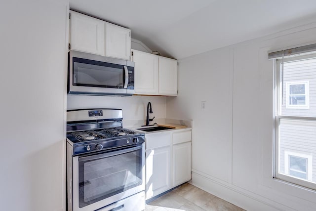 kitchen featuring sink, white cabinets, lofted ceiling, light tile patterned floors, and appliances with stainless steel finishes