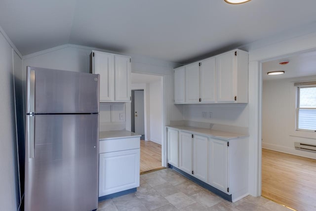 kitchen with white cabinets, vaulted ceiling, light hardwood / wood-style floors, and stainless steel refrigerator