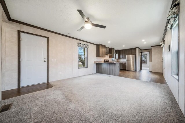 unfurnished living room with a textured ceiling, ceiling fan, dark hardwood / wood-style floors, and ornamental molding