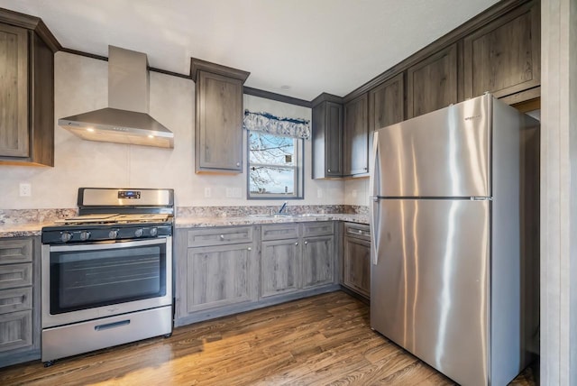 kitchen with light stone countertops, sink, wall chimney range hood, wood-type flooring, and appliances with stainless steel finishes