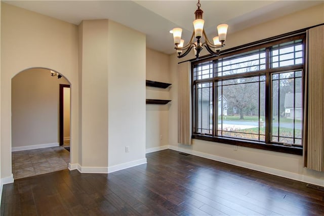 spare room with dark hardwood / wood-style floors and an inviting chandelier