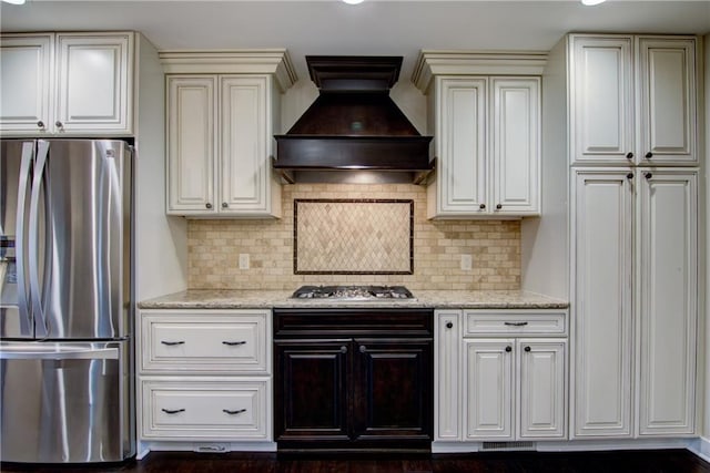 kitchen with appliances with stainless steel finishes, tasteful backsplash, light stone counters, and custom exhaust hood