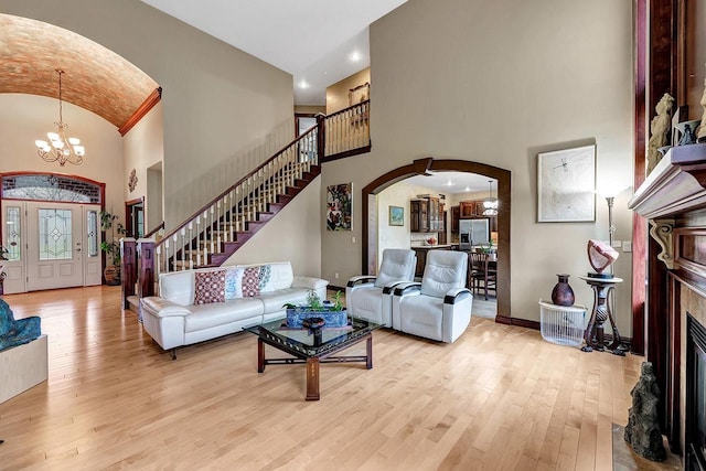 living room with a fireplace, high vaulted ceiling, light hardwood / wood-style floors, and an inviting chandelier