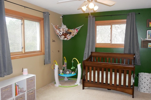 carpeted bedroom with a crib and ceiling fan