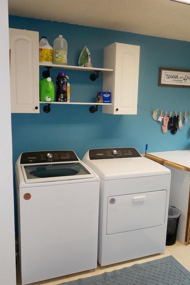 clothes washing area with cabinets, light tile patterned floors, and washer and dryer