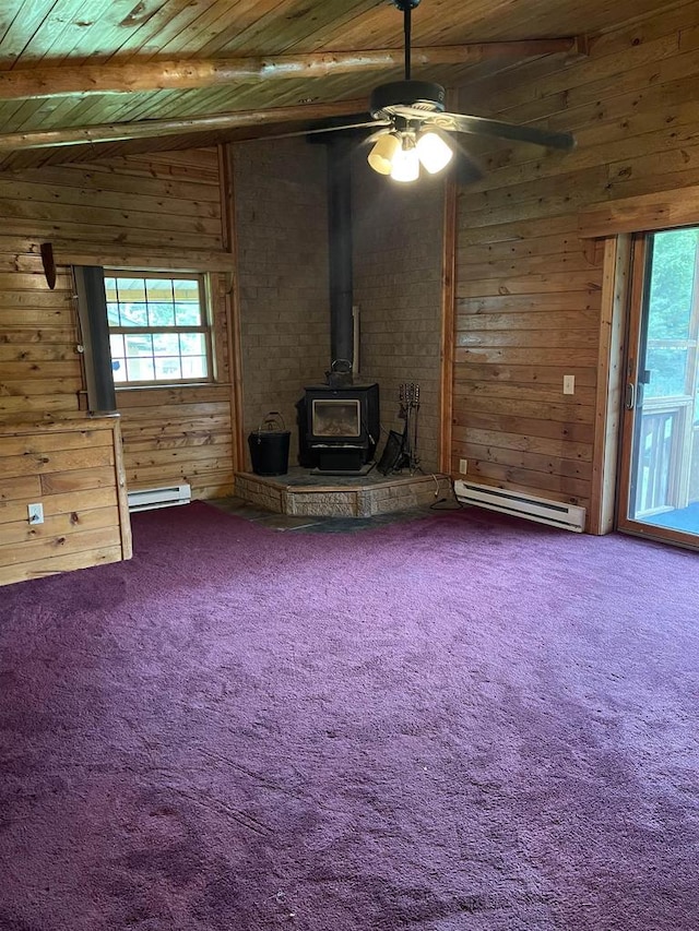 unfurnished living room with carpet flooring, a wood stove, baseboard heating, and a wealth of natural light