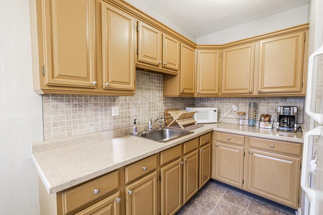 kitchen with tasteful backsplash, sink, dark tile patterned flooring, and white appliances