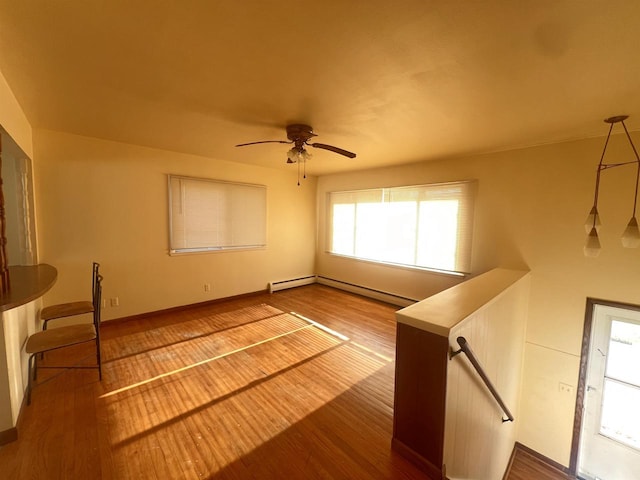 empty room featuring hardwood / wood-style floors, ceiling fan, baseboard heating, and a wealth of natural light