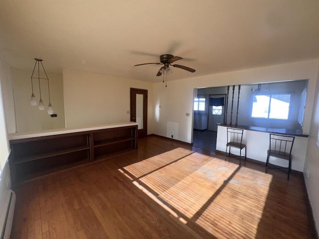 unfurnished living room featuring ceiling fan, dark wood-type flooring, and a baseboard heating unit