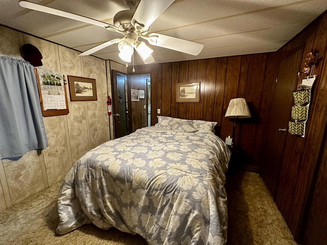 bedroom with ceiling fan, wooden walls, and carpet floors