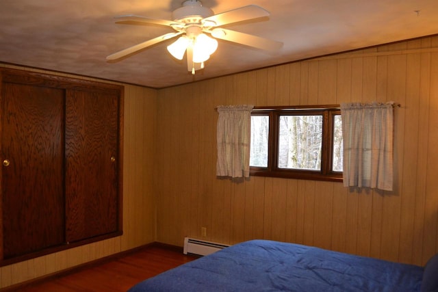 bedroom with baseboard heating, ceiling fan, dark hardwood / wood-style flooring, and wood walls