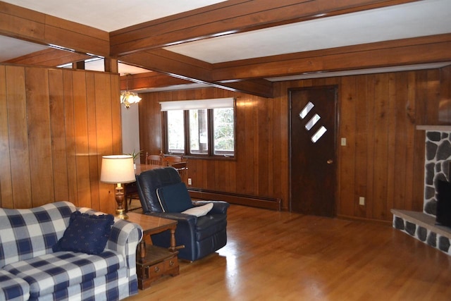 living room featuring baseboard heating, wooden walls, hardwood / wood-style flooring, beamed ceiling, and a stone fireplace