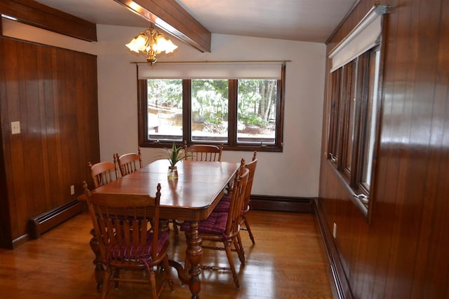 dining space featuring a baseboard radiator, an inviting chandelier, vaulted ceiling with beams, wood walls, and light wood-type flooring